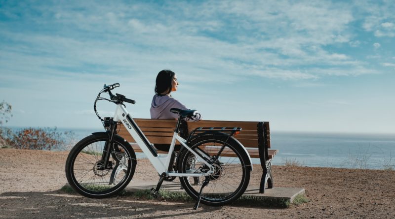man in black shirt sitting on brown wooden bench beside black and white bicycle during daytime