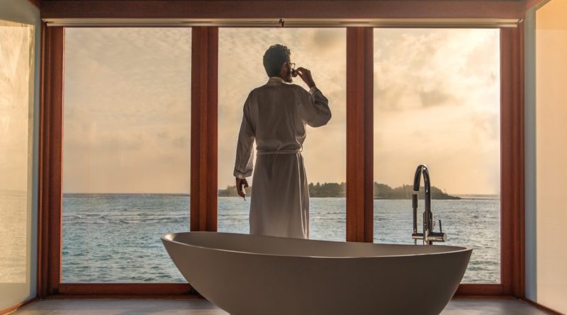 man standing in bathroom with bathtub next to body of water