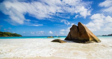 brown rock formation on sea shore under blue and white sunny cloudy sky during daytime