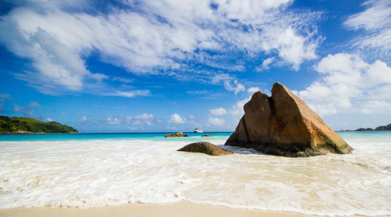 brown rock formation on sea shore under blue and white sunny cloudy sky during daytime