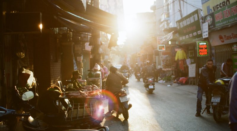 man holding motorcycle on road between buildings