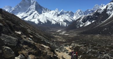 person in red jacket and black pants walking on rocky mountain during daytime