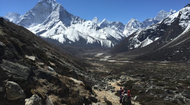 person in red jacket and black pants walking on rocky mountain during daytime